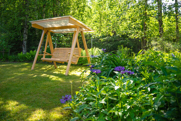 Wooden garden swing in a green garden in summer, relax in nature, landscape design - obrazy, fototapety, plakaty