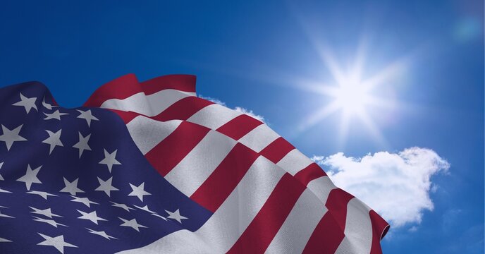 Composition of billowing american flag over sun in cloudy blue sky
