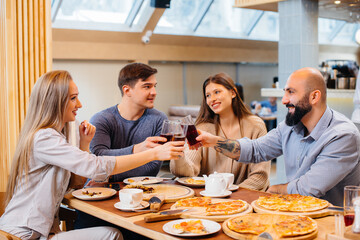 A group of young cheerful friends is sitting in a cafe talking and eating pizza. Lunch at the pizzeria.