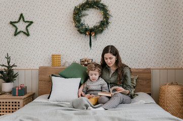 Woman and boy reading book on bed on Christmas day