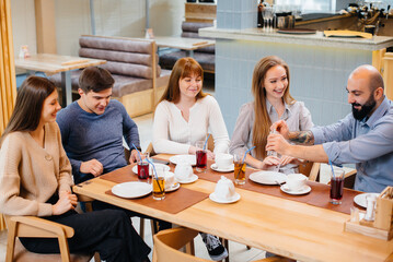 A group of young cheerful friends is sitting in a cafe talking and eating pizza. Lunch at the pizzeria.