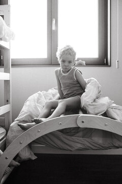 Little blond child sitting on a rainbow pikler with his duvet and looking bored