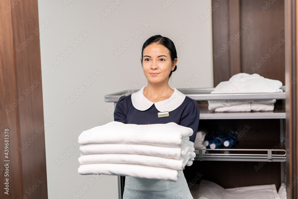 Poster Pretty room service staff holding clean sheets while standing by open door