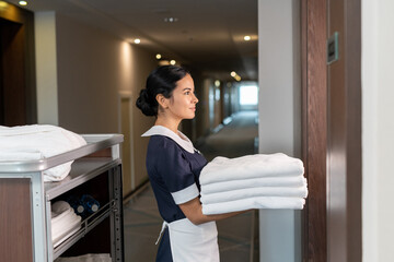 Fototapeta na wymiar Young chambermaid bringing clean sheets to one of hotel clients