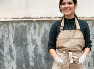 Portrait of a young ceramist woman with  hands dirty of clay in front of a wall