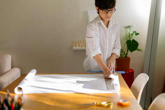 Front view of a pre-teen Boy starting a design project and unrolling a white roll paper