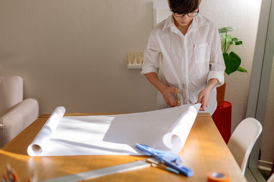 Front view of a pre-teen Boy starting a design project and unrolling a white roll paper