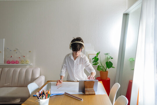 Pre-teen Boy wearing headphones drawing a map while using iPad on a table
