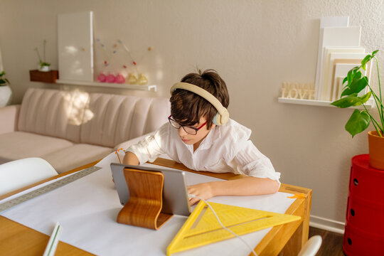 Boy in headphones drawing a map while using iPad at table