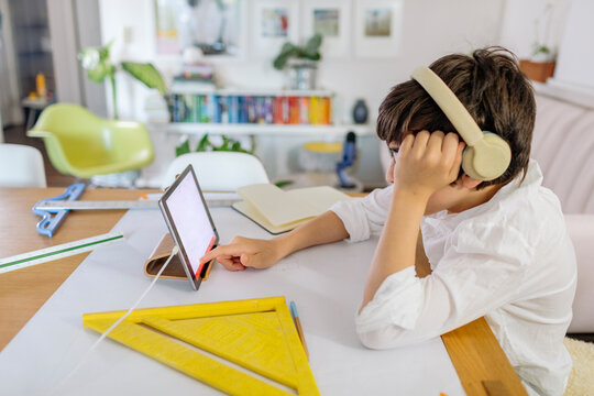Concentrate pre-teen designing a project  on paper and using a tablet sitting at table