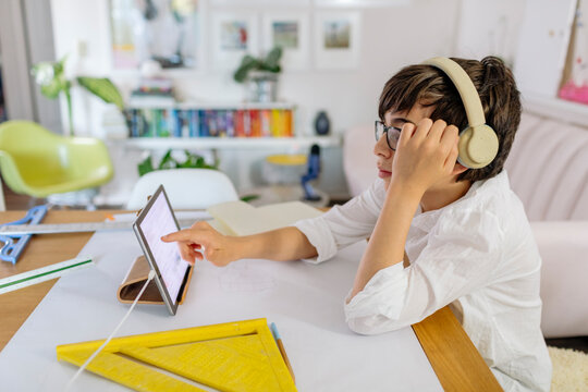 Concentrate pre-teen designing a project  on paper and using a tablet sitting at table