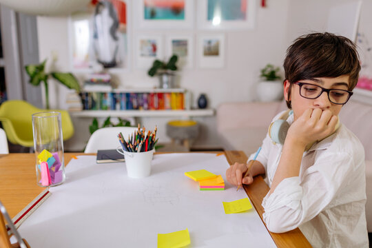 Pre-Teen Boy wearing white shirt writing on a stick note for his gratitude jar