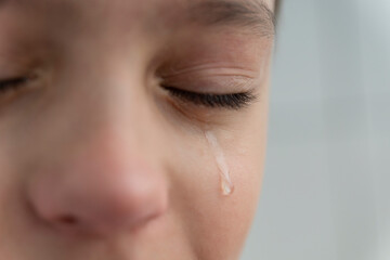 Tear rolls down the boy's cheek, his eyes are closed, he is upset and crying. Sad, unhappy emotions of child.