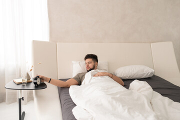 Obraz premium Young man stopping alarm clock in the morning while lying in bed