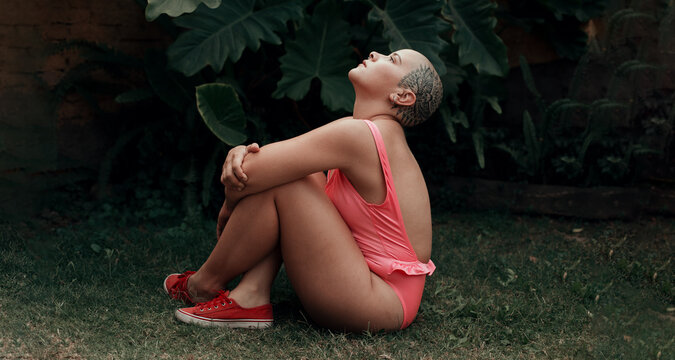 Emotional portrait of a beautiful bald woman with tattoo on her head, posing in a garden