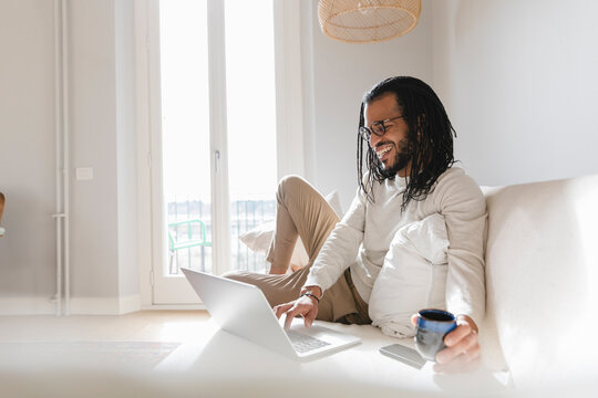Smiling man lying on the sofa while using his laptop