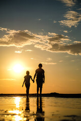 Silhouette of two sisters holding hands who standing on the beach at the sunset. Vertical photo
