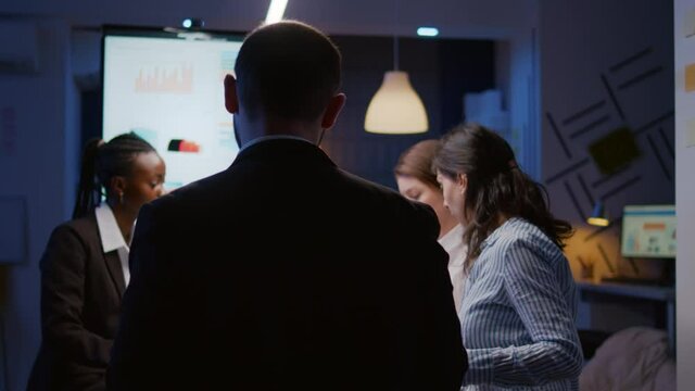 Selective focus of workaholics businesspeople brainstorming financial company ideas analyzing strategy paperwork late at night in business office meeting room. Multi-ethnic coworkers checking solution