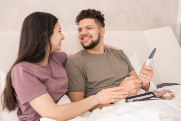 Happy future parents looking at one another while sitting in bed