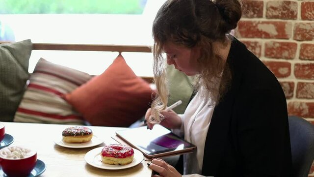 Girl in a cafe makes a sketch on an electronic tablet
