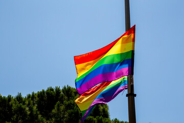 Rainbow flags hanging on a pole and waving on the air with blue sky background. LGBTQ community. Flags - Six-stripes version