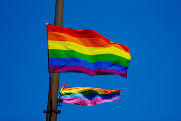 Rainbow flags hanging on a pole and waving on the air with blue sky background. LGBTQ community....