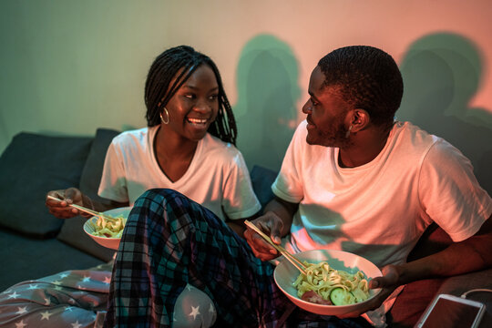 Happy Couple Eating On The Couch At Night. 