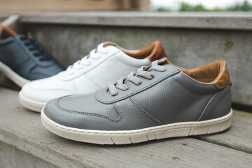 A pair of grey leather sneakers on wooden stairs for a monochromatic fashion image of Mens leather footwear and shoes.