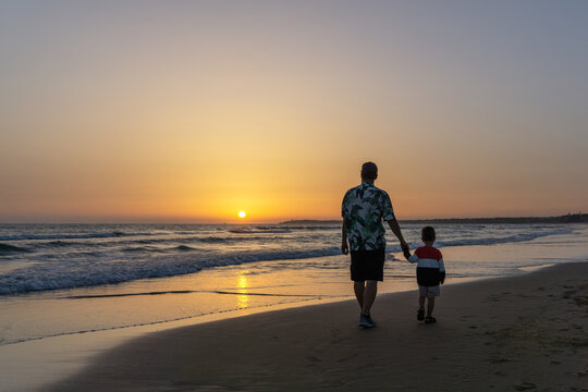 Father with his son walking on the beach at sunset