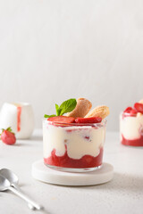 Layered strawberry dessert with cookie savoyardi, mascarpone and whipped cream decorated strawberries on white background. Close up. Vertical format.