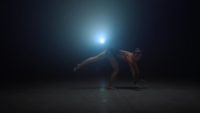 Athletic woman doing handstand in dark studio. Flexible gymnast training indoors
