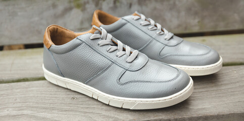 A pair of grey leather sneakers on wooden stairs for a monochromatic fashion image of Mens leather footwear and shoes.