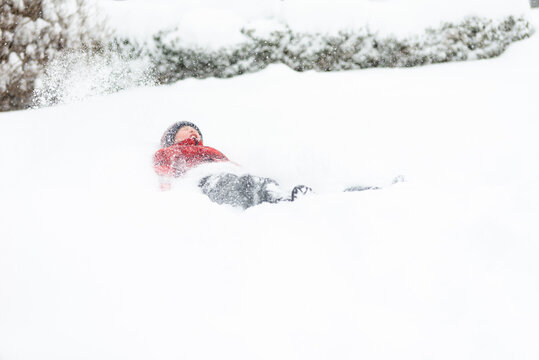 Boy Jumping Into Snow in Snowy Suburban Yard During Winter Snowfall