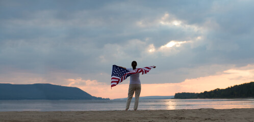 a woman with an American flag on the ocean at sunset. Independence Day. The United States celebrates July 4.
