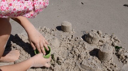 Toddler plays with sand molding toy on wet beach sand by sea coastline. Child makes sand molds. Summer kids games at seaside