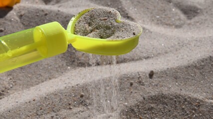 Sand grains pouring through sand sifter. Yellow plastic toy sand sifter in shape of heart. Games...