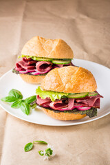 Ready-to-eat hamburgers with pastrami, vegetables and basil on a plate on craft paper. American fast food. Vertical view