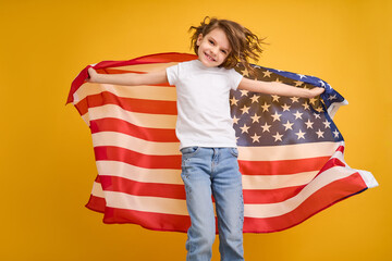 Happy child, cute girl with American flag on yellow studio background. USA celebrate July 4th, independence Day.