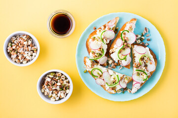 Ready-to-eat bruschetta with curd cheese, vegetables and sprouted grains on a plate on a yellow background. Healthy snacks. Top view