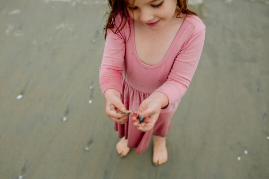 Barefoot girl in pink dress holding seashells