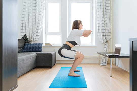 woman doing squats in front of laptop at home