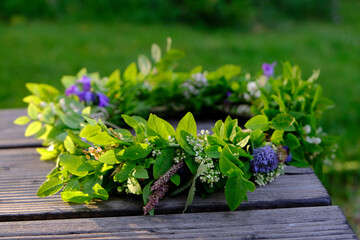 Fresh wreath of flowers and bright green branches on a wooden table, sunlit during the Solstice