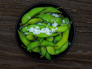 Top view of a bowl containing edamame beans with sea salt flakes
