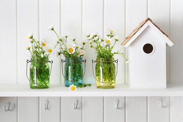 Glass jars of daisies on shelf with birdhouse