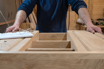 hands of a master carpenter who makes a handmade cabinet made of natural wood in light colors. Next to the glasses and the drawing. Production of custom-made furniture