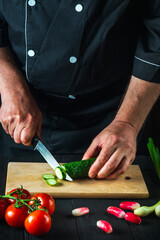 Professional chef cuts a green cucumber on a restaurant kitchen cutting board for salad. Vegetable diet or snack idea