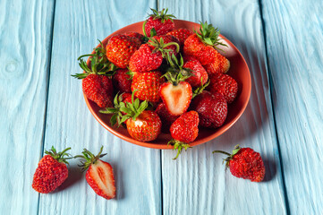 Full plate of strawberries and a cut piece on a blue table. Strawberry Diet Idea