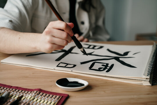 Young woman writing japanese kanji characters with a brush and ink