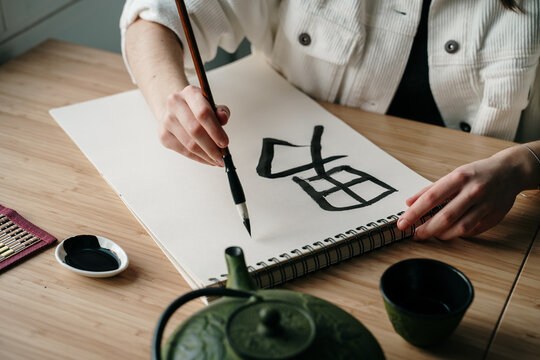Young woman writing japanese kanji characters with a brush and ink