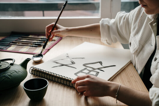 Young woman writing japanese kanji characters with a brush and ink